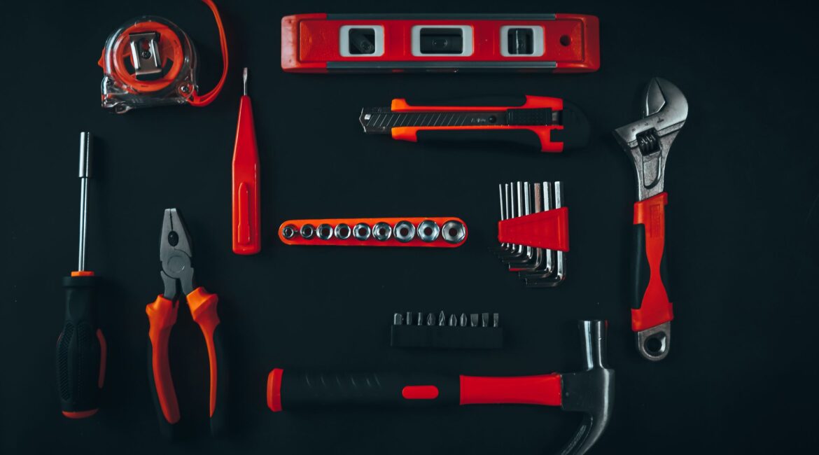 Hand tools neatly arranged on a dark workbench, including pliers, wrench, hammer, sockets and tape measure